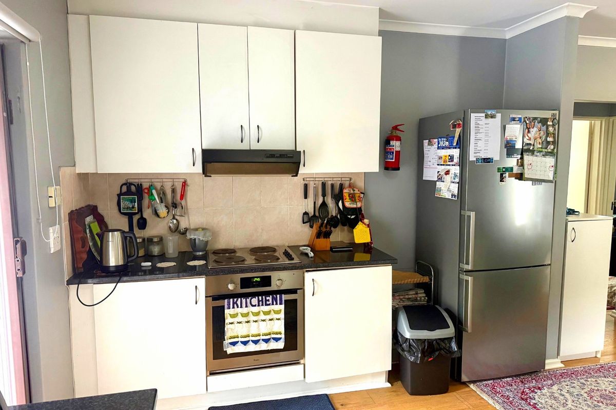 A functional kitchen featuring white cabinetry, a built-in oven with electric cooktop, extractor fan, and tiled backsplash, providing a practical cooking space.