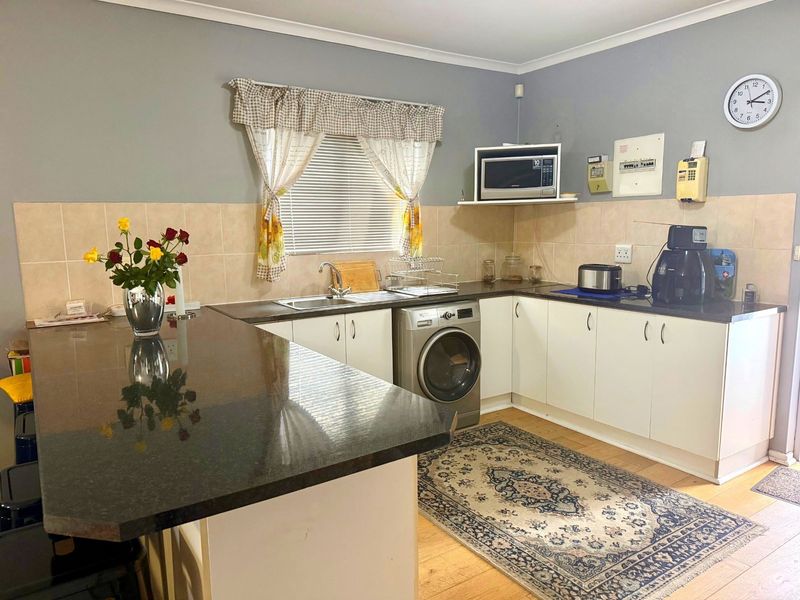 A functional kitchen featuring granite countertops, white cabinetry, tiled backsplash, and integrated space for laundry appliances.