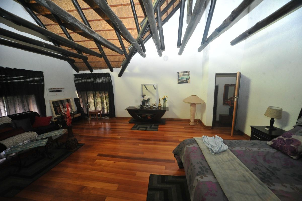 Spacious bedroom featuring high vaulted ceilings with exposed timber rafters, a traditional thatched roof, and warm hardwood flooring.