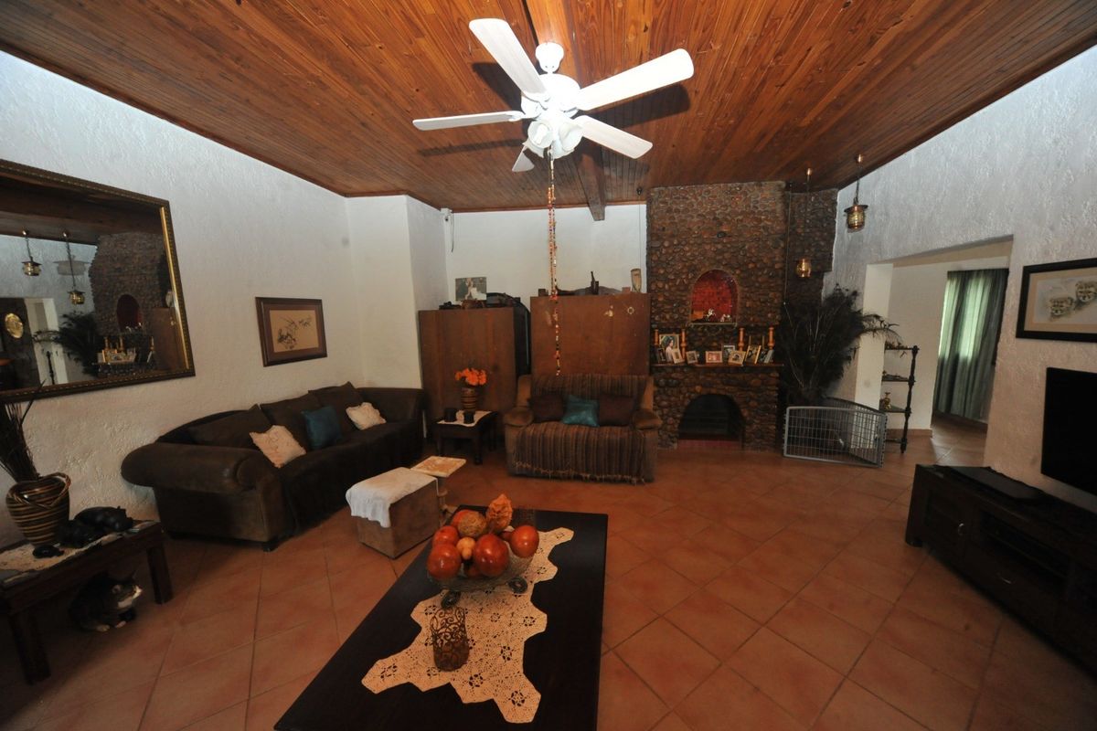 Spacious living room featuring a rustic stone fireplace, warm timber ceiling, and tiled flooring, offering a cozy atmosphere for relaxation.