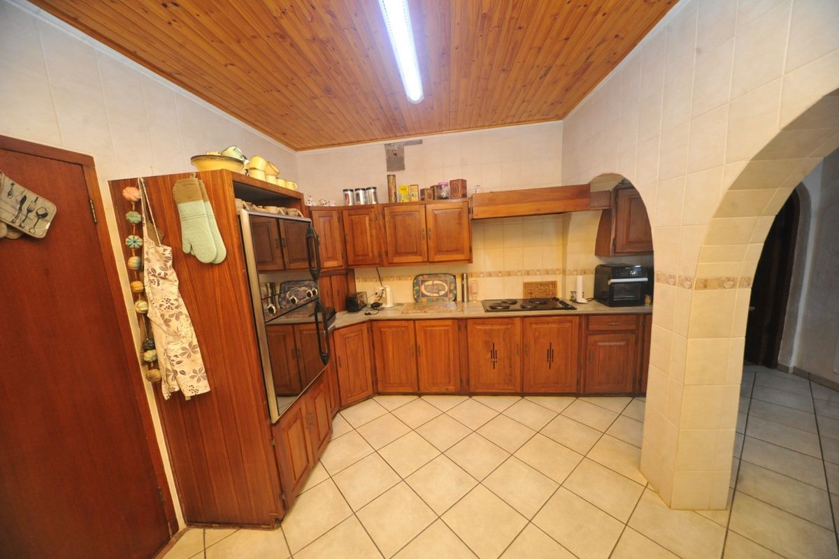 A traditional kitchen featuring wooden cabinetry, built-in oven, hob, tiled flooring, and a distinctive wooden ceiling with an arched entryway.