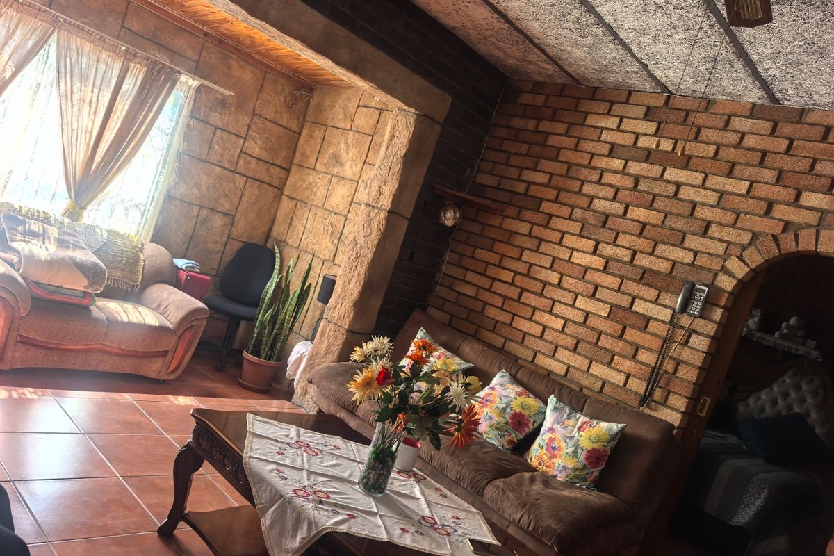 A living room featuring exposed brick walls, tiled flooring, and timber ceiling beams, offering a rustic aesthetic with an arched doorway leading to adjacent spaces.