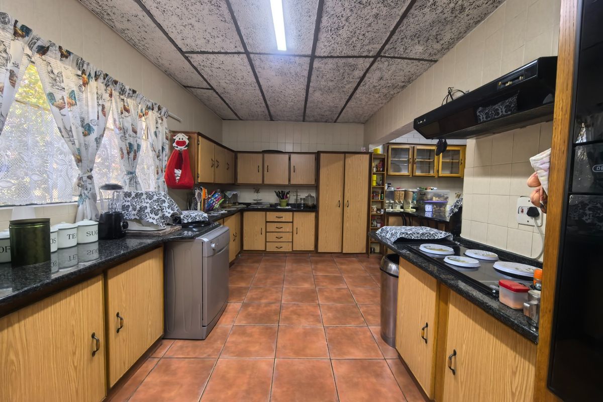 A spacious kitchen featuring laminate cabinetry, granite countertops, built-in oven, electric hob, and tiled flooring, offering a functional layout with significant renovation potential.