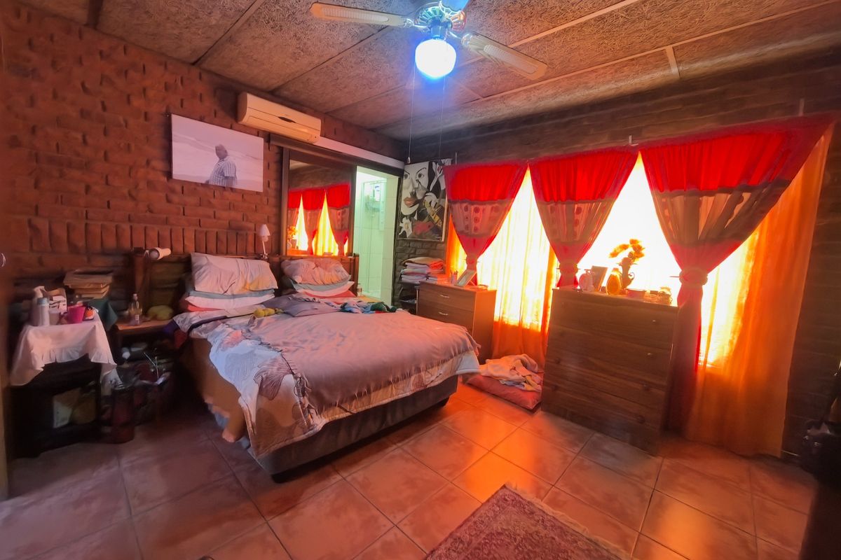 A bedroom featuring exposed brick walls, tiled flooring, a ceiling fan, and a wall-mounted air conditioning unit.