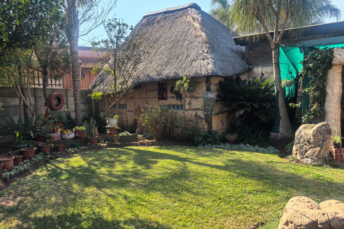 A rear garden view featuring a traditional thatched-roof structure, established landscaping, and a boundary wall in a residential setting.