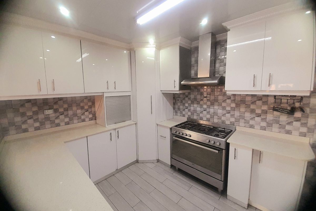Modern kitchen featuring white gloss cabinetry, stone countertops, a stainless steel gas stove with extractor fan, and a tiled backsplash.