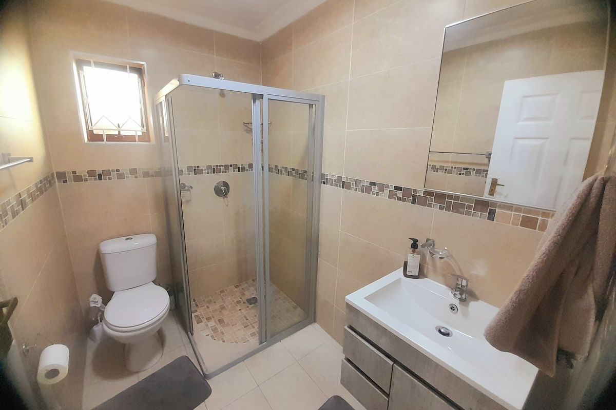 A functional bathroom featuring a glass shower enclosure, a modern vanity cabinet with a basin, and neutral wall and floor tiling.
