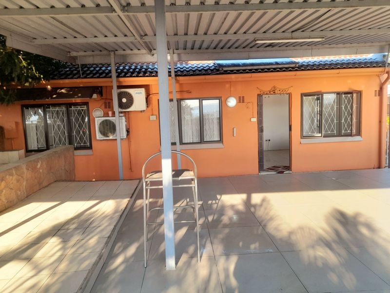 A covered outdoor patio area featuring tiled flooring, metal roofing, and security-barred windows, providing a functional space for outdoor living.
