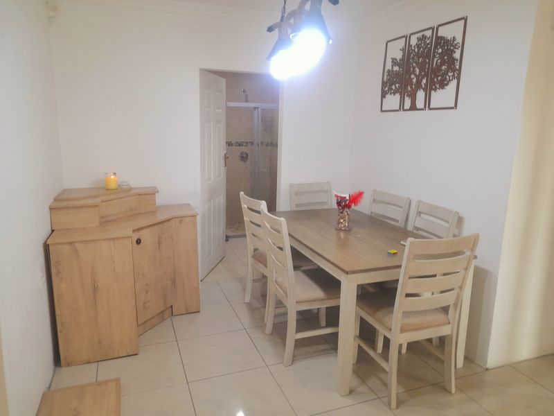 A dining area featuring tiled flooring and pendant lighting, with a view into an adjacent bathroom space.
