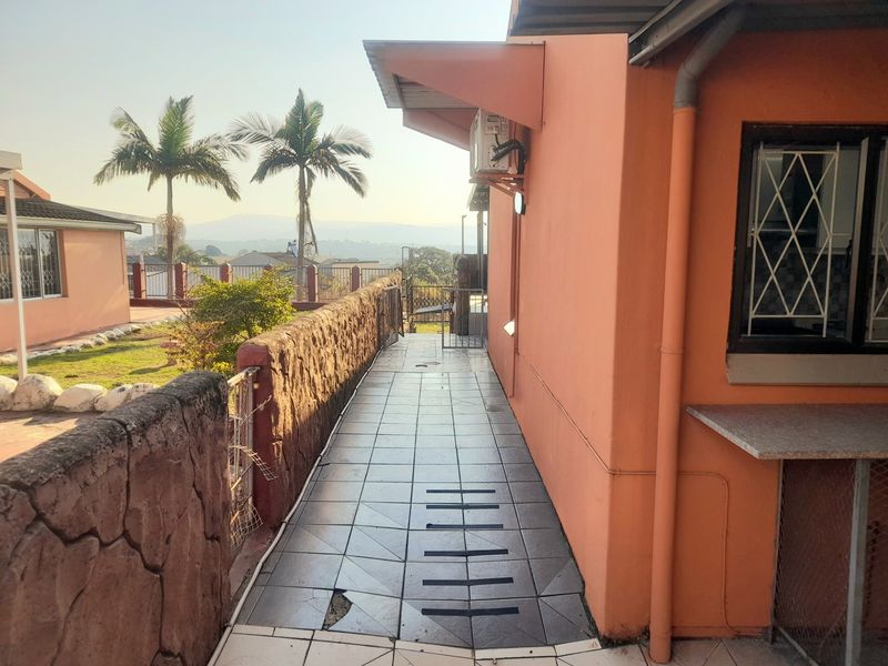 A tiled outdoor walkway area featuring a stone retaining wall, security gate, and exterior wall-mounted air conditioning unit.