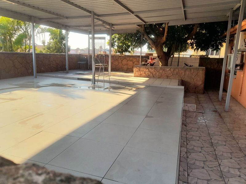 A spacious covered patio area featuring tiled flooring and a stone-clad retaining wall, offering a versatile outdoor space for relaxation or entertainment.