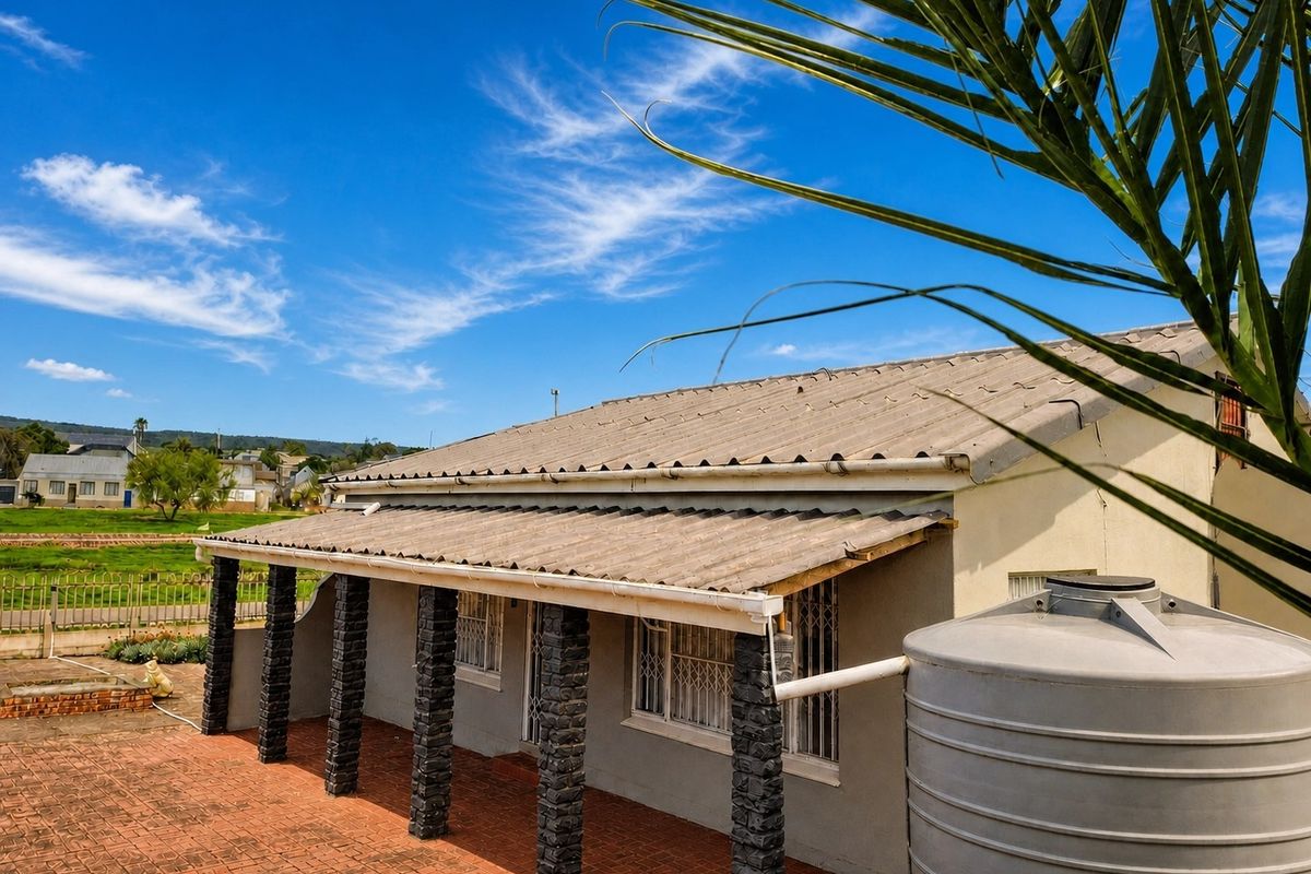 Rear exterior view of the house featuring a covered patio with stone-clad pillars, brick paving, and a rainwater collection tank.