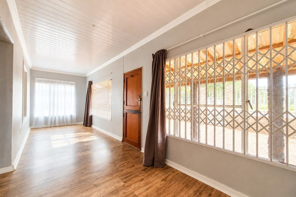 A bright, empty living area featuring laminate flooring, a timber tongue and groove ceiling, and security gates on the windows.
