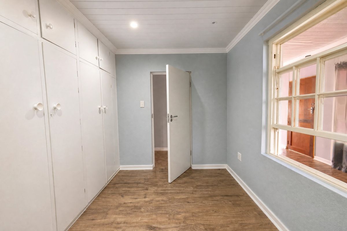 A bright, empty bedroom featuring built-in cupboards, timber-look flooring, and a classic timber-paneled ceiling with a view into an adjacent room.