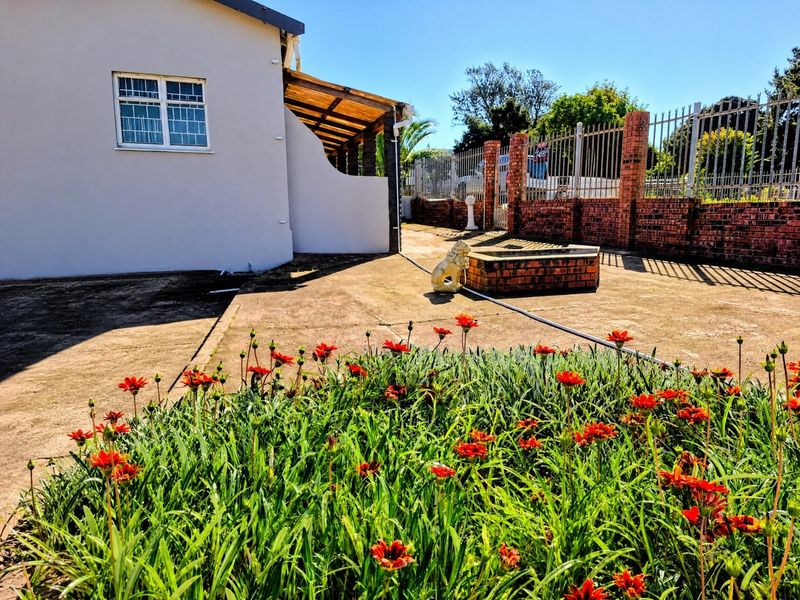 Rear exterior view featuring a concrete patio, brick boundary wall with metal fencing, and a small brick planter box in the garden area.