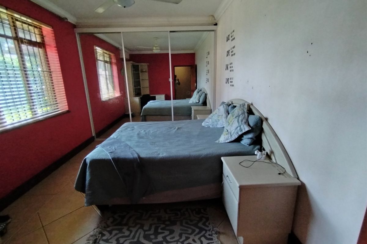 A bedroom featuring tiled flooring, a ceiling fan, and a large mirrored sliding wardrobe, offering functional storage space.