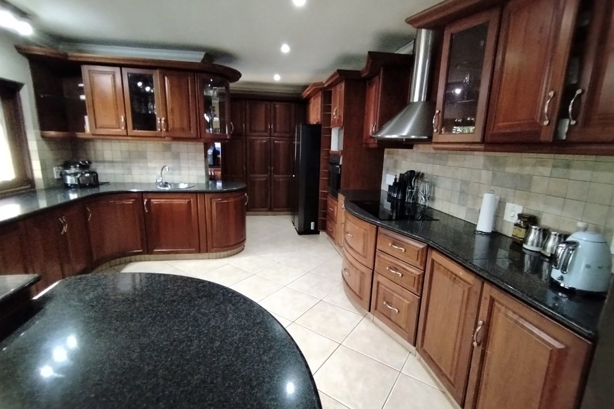 Spacious kitchen featuring dark wood cabinetry, granite countertops, a stainless steel extractor fan, and tiled flooring with ample storage space.