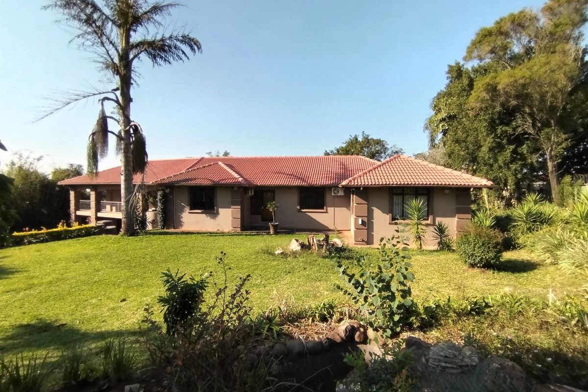 A well-maintained single-story house featuring a terracotta tiled roof, stucco exterior, and a spacious rear garden with a covered patio area.