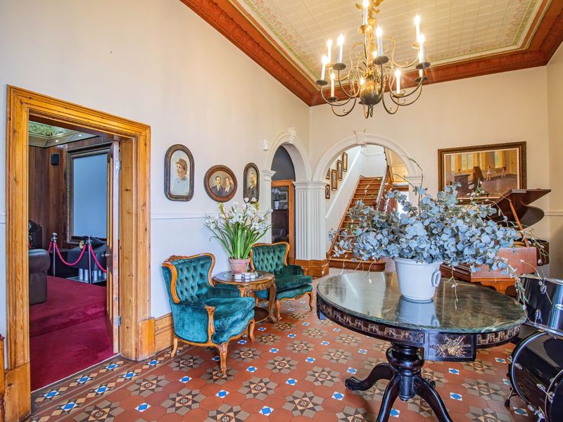 Grand entrance hall featuring ornate ceiling details, a classic chandelier, and decorative tiled flooring, leading to an internal staircase and adjacent rooms.