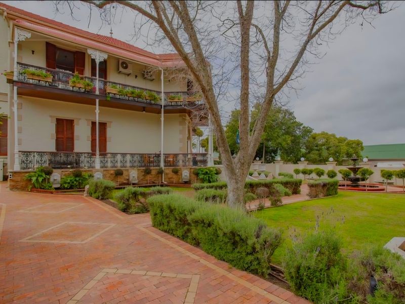 A well-maintained rear exterior view featuring a multi-level balcony with wrought iron detailing, brick paving, and a landscaped garden with a central water fountain.