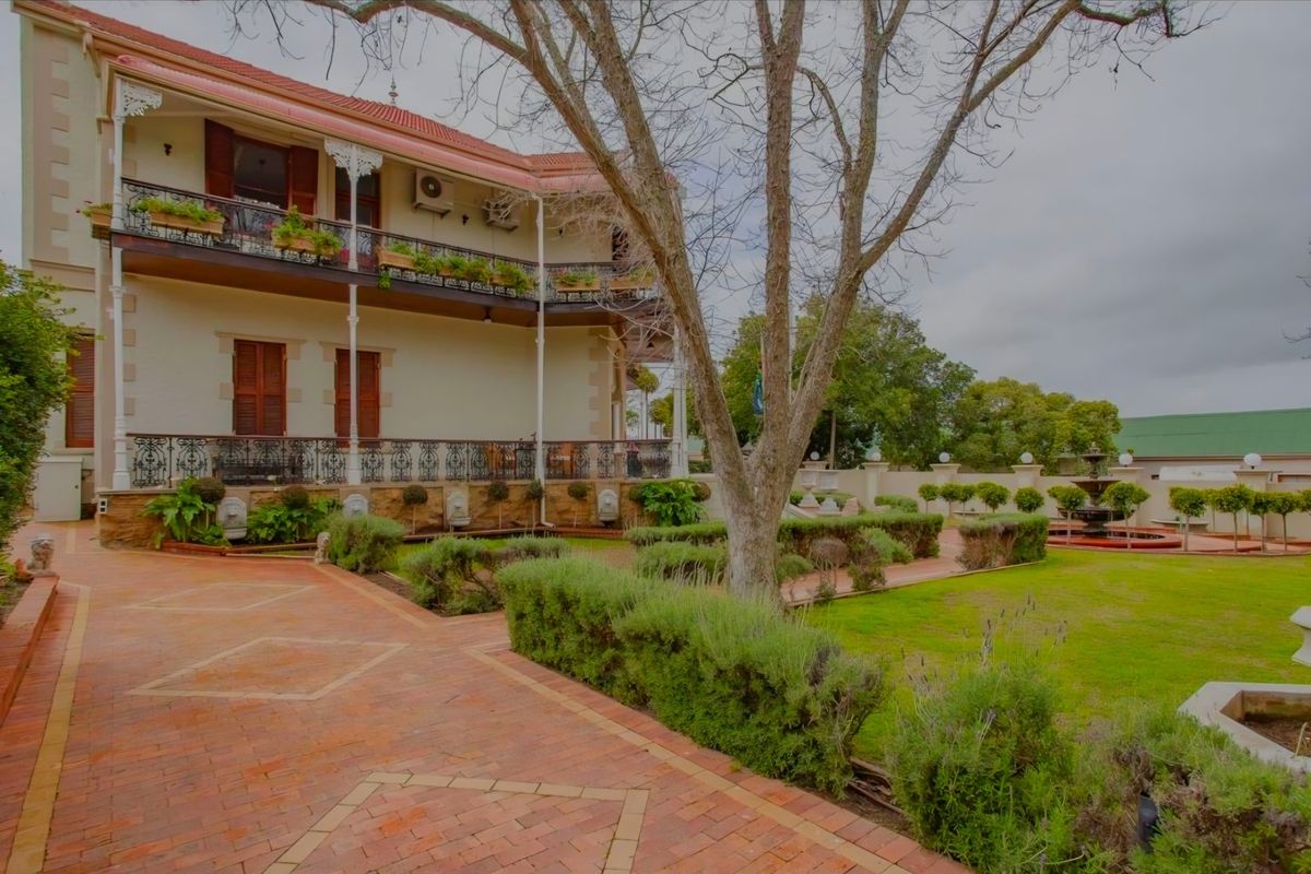 A well-maintained rear exterior view featuring a multi-level balcony with wrought iron detailing, brick paving, and a landscaped garden with a central water fountain.