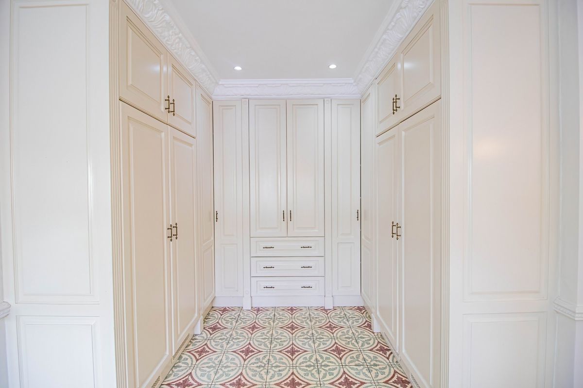 A well-appointed walk-in closet or dressing area featuring extensive built-in cabinetry, decorative crown molding, and elegant patterned floor tiles.
