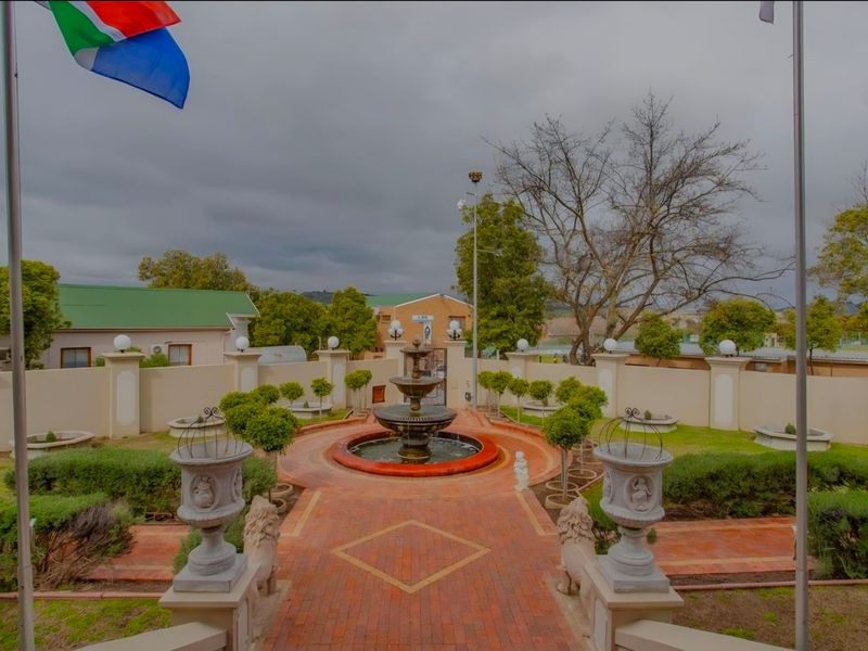 A well-maintained garden featuring a central tiered water fountain, brick-paved pathways, and a secure perimeter wall with integrated lighting.