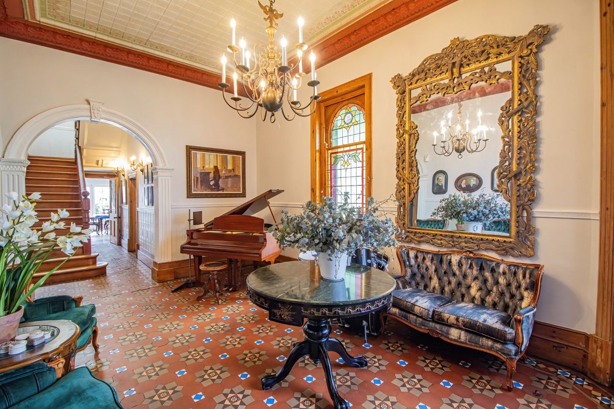 Elegant living area featuring intricate tiled flooring, ornate ceiling details, stained glass windows, and a grand archway leading to a wooden staircase.