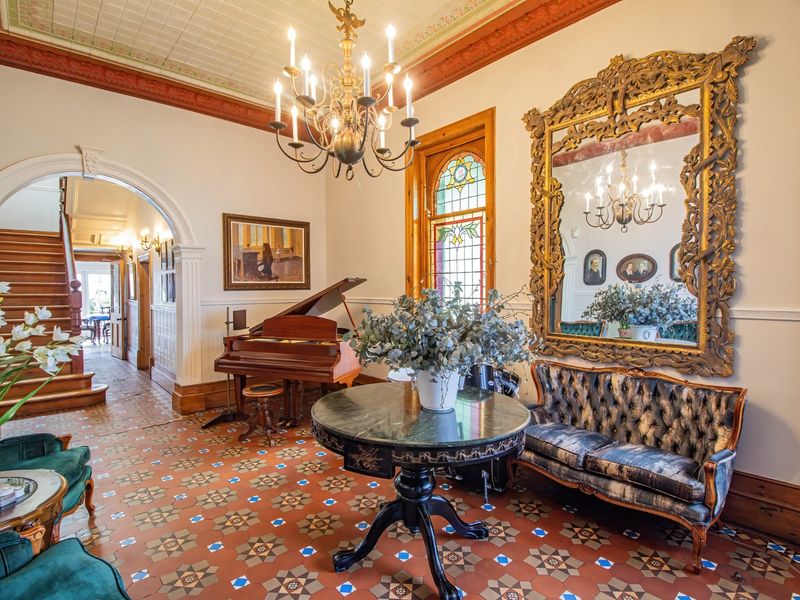 Elegant living area featuring intricate tiled flooring, ornate ceiling details, stained glass windows, and a grand archway leading to a wooden staircase.