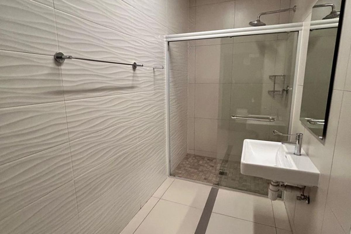 Modern bathroom featuring a walk-in shower with glass enclosure, wall-mounted basin, and contemporary textured wall tiling.