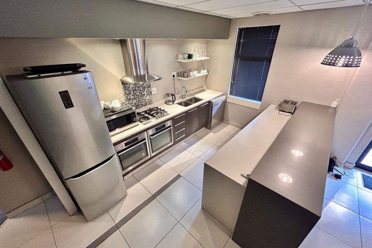 Modern commercial kitchen featuring stone countertops, built-in oven, gas hob, stainless steel extractor fan, and tiled flooring with ample cabinetry.