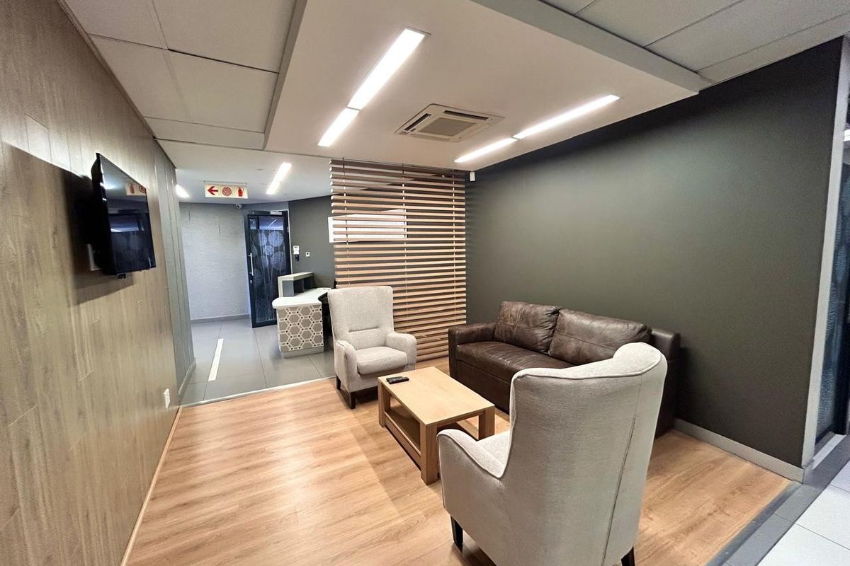 A modern commercial lounge area featuring wood-look flooring, a timber slat partition, recessed ceiling lighting, and a sleek wood-panelled feature wall.