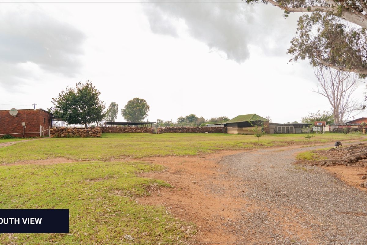 A wide-angle view of the farm grounds featuring a gravel driveway, open lawn area, and various brick and metal outbuildings.
