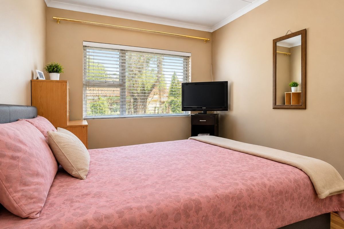 A well-lit bedroom featuring neutral wall tones, laminate flooring, and venetian blinds, offering a comfortable and functional living space.