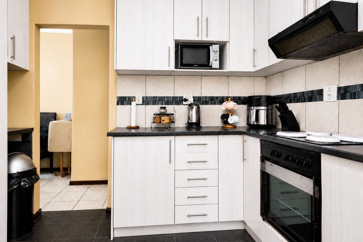 A functional kitchen featuring white cabinetry, dark countertops, built-in oven with extractor fan, and a tiled backsplash, leading into an adjacent living area.
