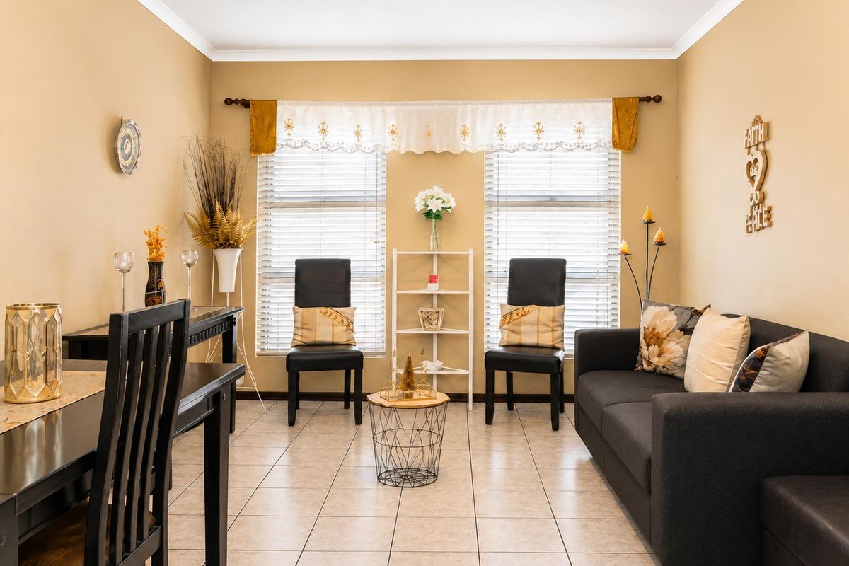 A well-lit living area featuring neutral tiled flooring, dual windows with venetian blinds, and classic cove cornicing.