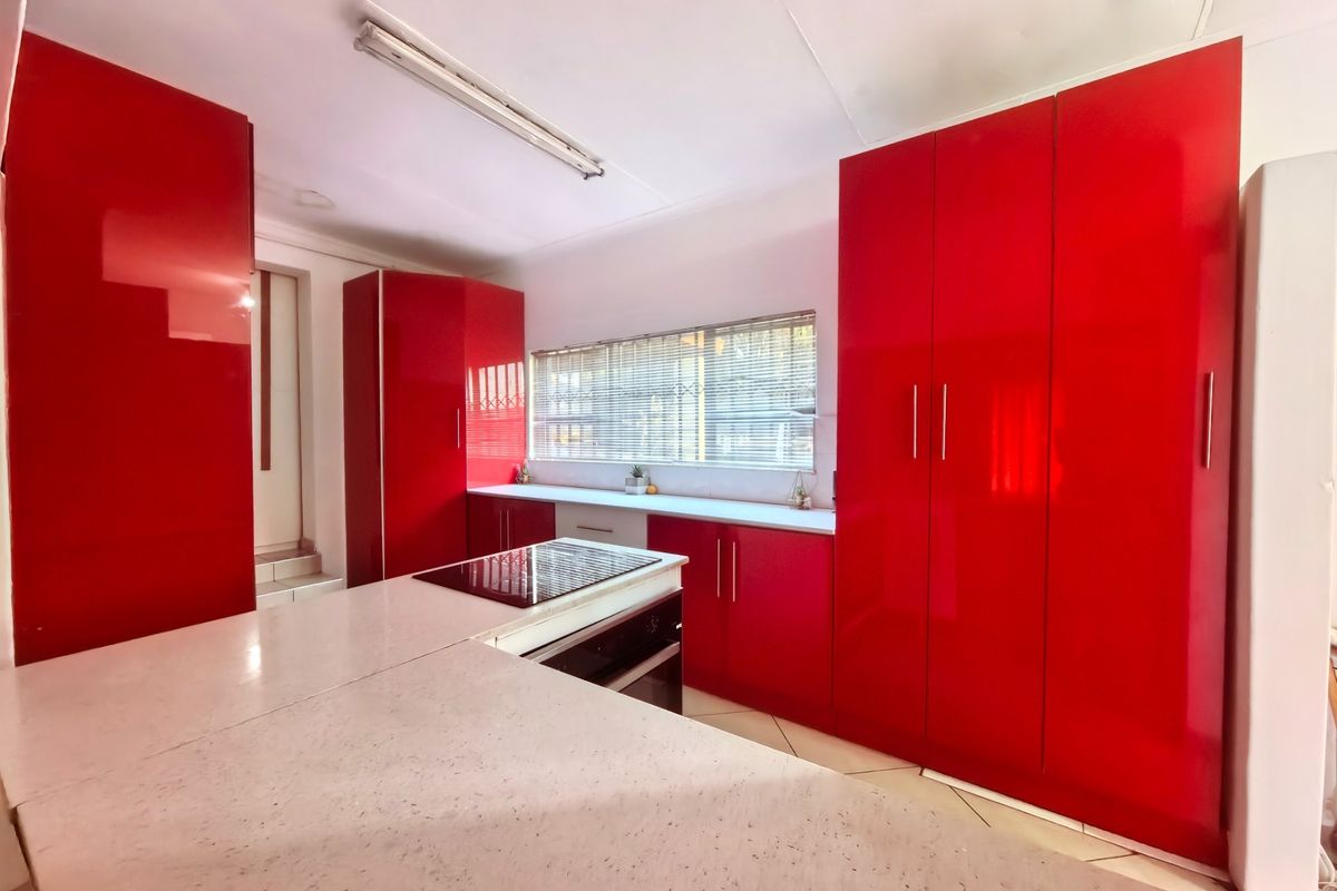 Modern kitchen featuring striking high-gloss red cabinetry, stone countertops, and integrated cooking appliances, offering a clean and functional workspace.