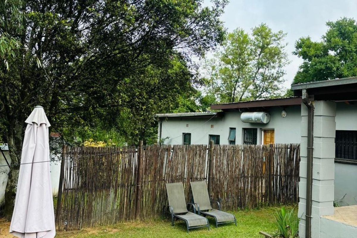 A rear garden area featuring a lawn, reed fencing, and a view of the building exterior with a mounted solar water heater.