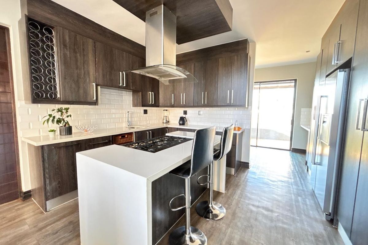 Modern kitchen featuring dark wood cabinetry, white stone countertops, subway tile backsplash, and a central island with a built-in gas hob.