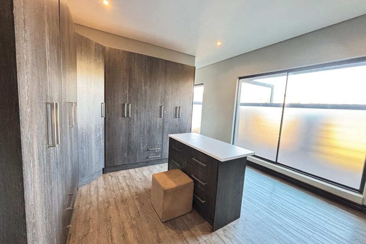 A modern dressing room or bedroom featuring extensive dark wood built-in cabinetry, laminate flooring, and a large window with frosted glass for privacy.