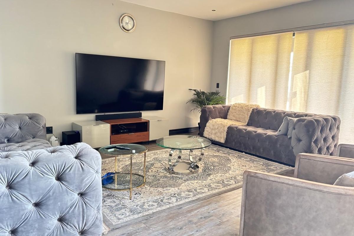 A well-maintained living room featuring modern recessed downlights, durable laminate flooring, and large windows fitted with roller blinds.