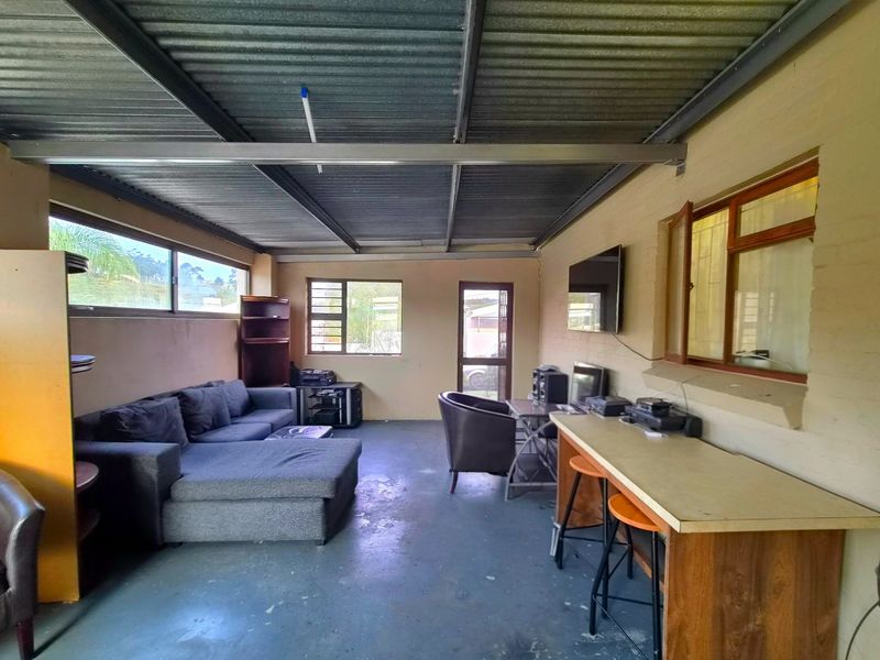 A covered outdoor patio area featuring a corrugated metal roof, exposed steel beams, and concrete flooring, suitable for conversion into an entertainment space.