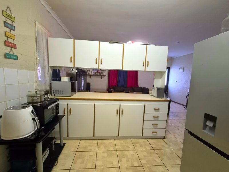 A functional kitchen featuring white cabinetry, laminate countertops, and tiled flooring, offering a dated aesthetic with potential for modern renovation.