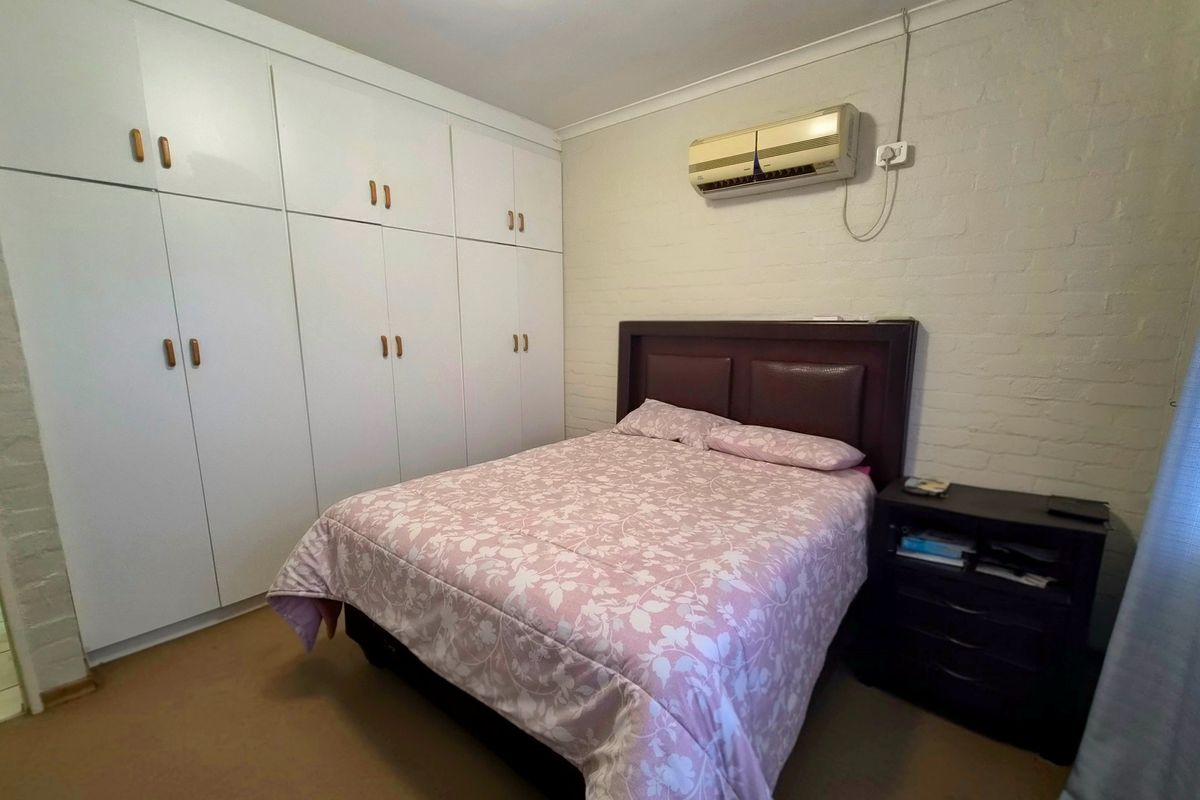 A bedroom featuring built-in cupboards, a painted brick wall, and a wall-mounted split-system air conditioner.