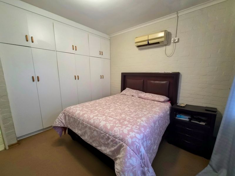 A bedroom featuring built-in cupboards, a painted brick wall, and a wall-mounted split-system air conditioner.