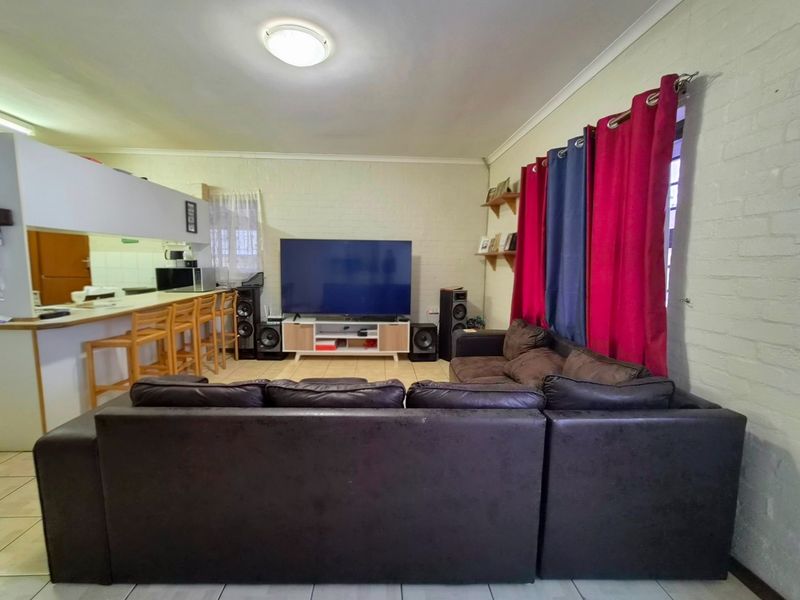 Open plan living area featuring tiled flooring, painted brick walls, and a breakfast bar connecting to the kitchen space.