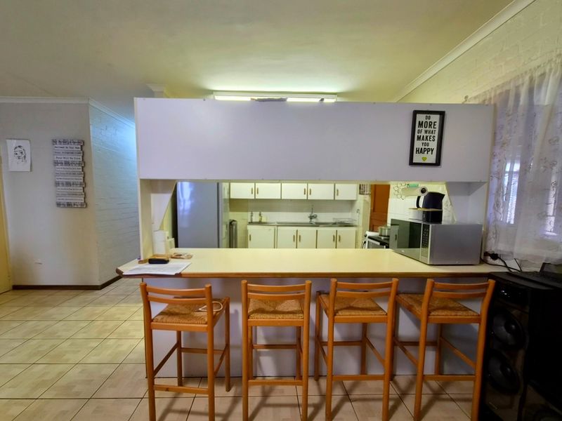 Open plan living area featuring a breakfast bar overlooking a functional kitchen with built-in cabinetry and tiled flooring throughout.