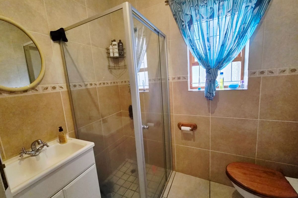 A functional bathroom featuring a shower enclosure, vanity basin, and toilet with neutral wall and floor tiling.