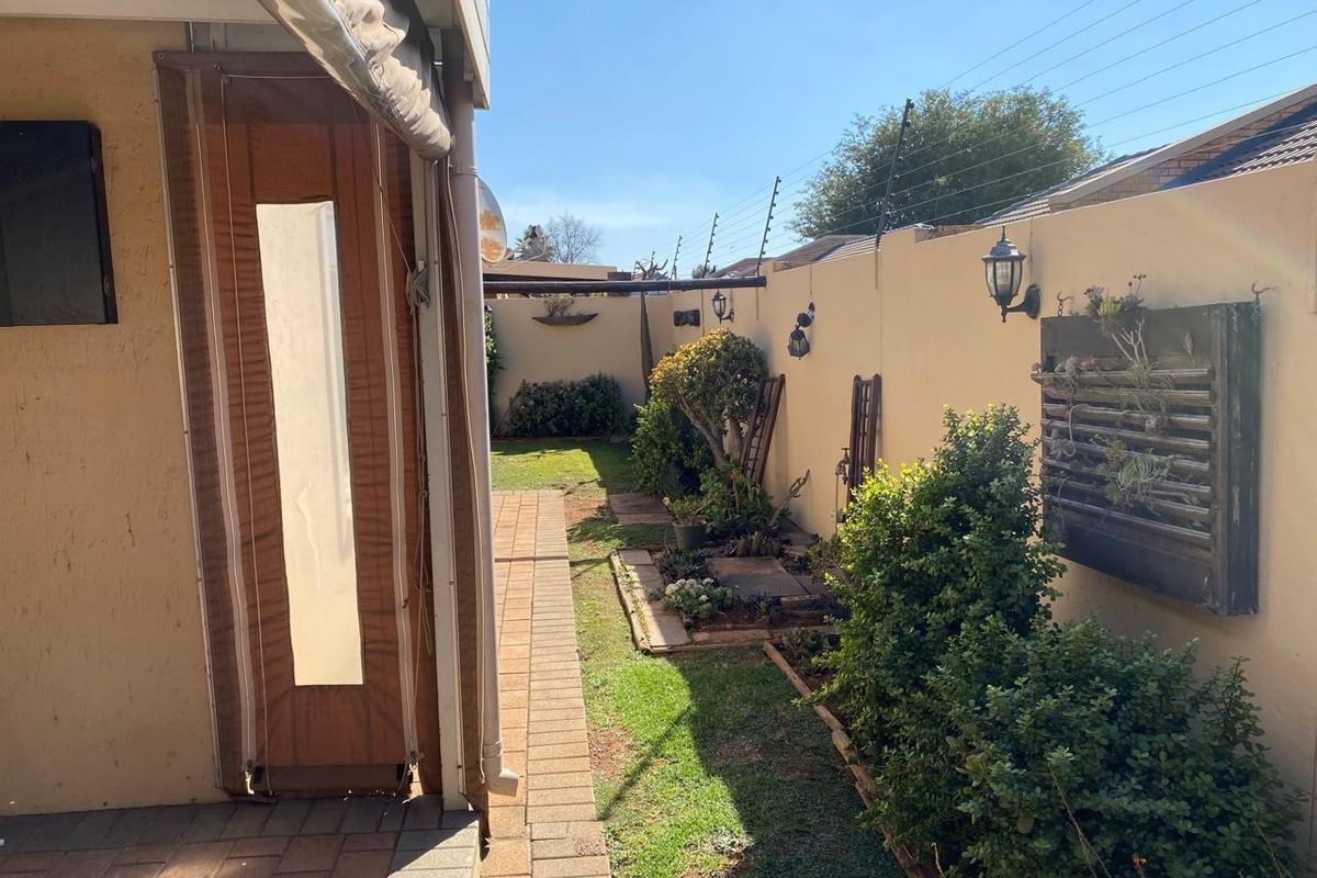 A well-maintained rear garden area featuring a paved walkway, boundary wall with electric fencing, and outdoor lighting, providing a private and secure outdoor space.