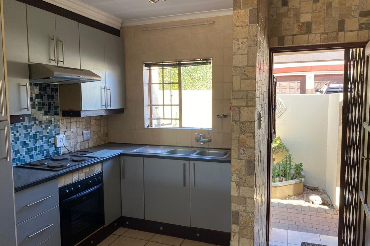 Compact kitchen featuring built-in cabinetry, electric hob, oven, and a stone-clad feature wall with direct access to an outdoor area.